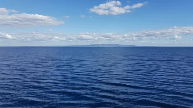 Calm blue sea under a bright sky with some clouds in the distance
