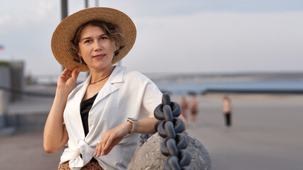 Smiling woman posing stylishly in straw hat seaside evening.