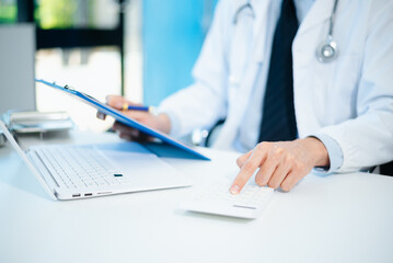 Healthcare costs and fees concept.Hand of smart doctor used a calculator and smartphone, tablet for medical costs at hospital
