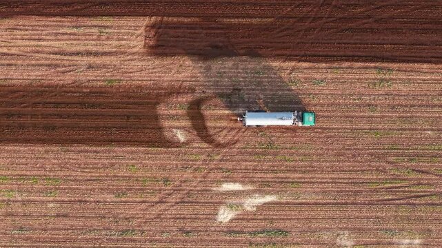 Aerial view of a truck spraying manure on an agricultural field to fertilize the soil, creating patterns on the farmland surface.
