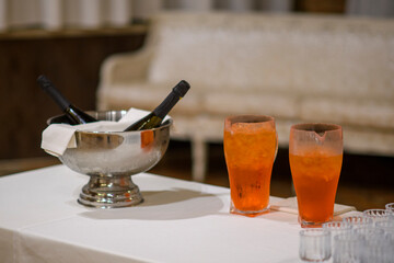 Elegant Evening Celebration Toast with Chilled Wine Bottles and Orange Cocktails Set on a White Tablecloth Ready for Guests Arriving Soon