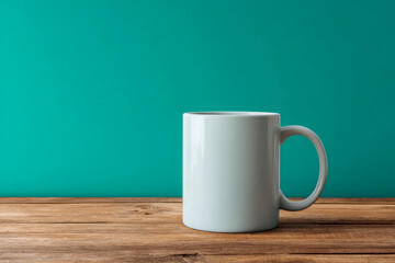 Plain white ceramic mug with handle placed on wooden surface against teal green background for coffee or tea use