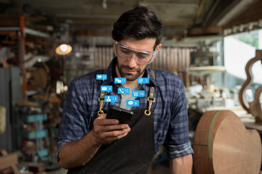 Carpenter checking smartphone with social media notifications in workshop showing digital lifestyle