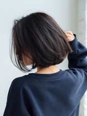 Fototapeta premium Back view of a person wearing a blue sweater with short dark hair adjusting their hair, showcasing a simple and stylish hairstyle.