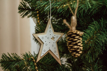beautifully decorated Christmas tree features wooden star ornament with white and gold details and rustic pine cone ornament. scene captures warmth holiday season. close up.