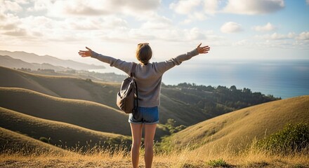 Woman standing with arms outstretched on a hill overlooking the ocean