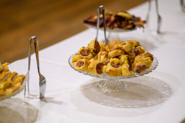 Delicious Savory Appetizers Buffet Served at a Celebration Event Featuring Bite Sized Sausage Rolls and Other Finger Foods on a White Tablecloth