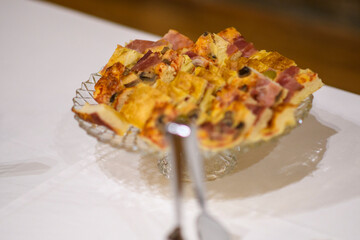 Delicious savory pie sliced on a glass plate with a fork about to take a piece presented on a white tablecloth for a delightful meal or party celebration