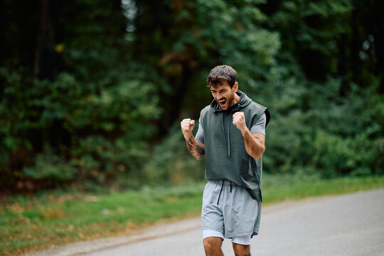 Man with clenched fists celebrating achievement and victory during his outdoor running workout, demonstrating fitness and determination