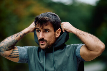 Athletic man pulling up hoodie, preparing for intense outdoor fitness training. Focused and...