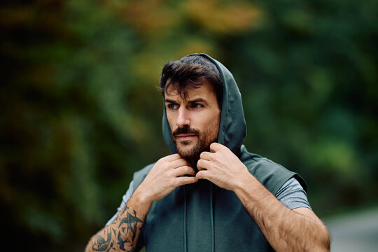 Young man with beard and tattoo preparing for fitness exercise. Runner focusing on his workout outdoors
