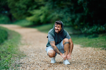 Young man adjusting running shoes on a trail, preparing for his outdoor workout in a natural park...
