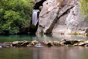 Tranquil nature landscape featuring a smooth waterfall, green pooling water, and ancient rock...