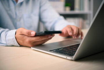 Businessman using mobile phone for online banking and two factor authentication on laptop. Security technology for payment and financial transaction. Man working with computer and smartphone.