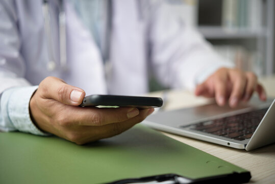 Doctor using mobile phone for telemedicine consultation. Medical professional with laptop providing online healthcare service for patient. Modern technology in medicine and health clinic.