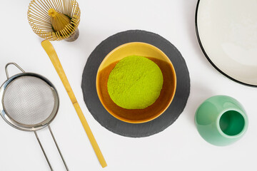 Matcha powder and chasen bamboo and brewing equipment on a background. Japanese traditional drink, top view.