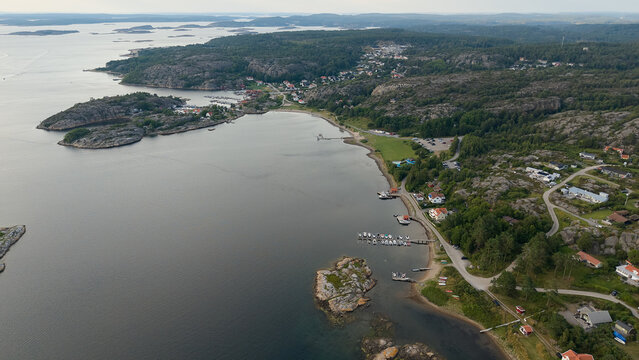Aerial View of Coastal Village Near Strömstad, Sweden with Rocky Hills, Waterfront Homes, Small Harbor, and Calm Sea on an Overcast Day