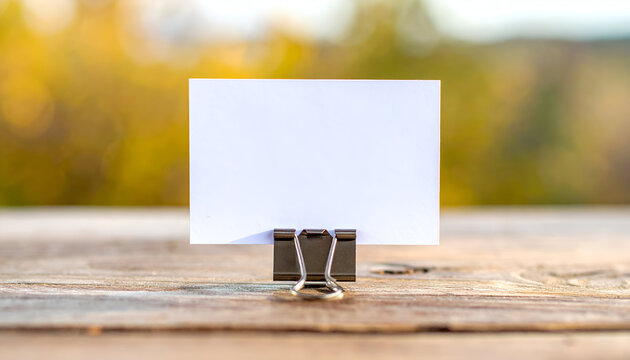 Blank business card stands on a wooden surface with blurred autumn foliage in the distance, creating a clean and minimalist scene for mockups.