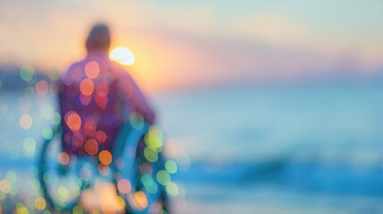 A person sits in a wheelchair, silhouetted against a colorful sunrise by the ocean. The warm light reflects on the water, creating a peaceful atmosphere