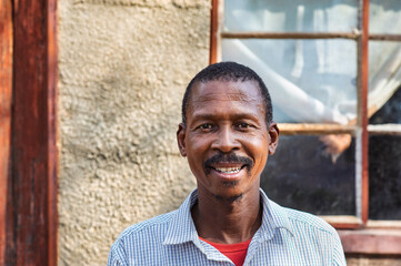 single african old man portrait, in the village, standing in front of the house, rural life in...