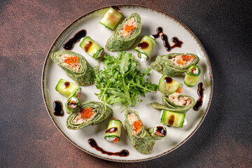Top view of spinach crepes with salmon and cucumber rolls