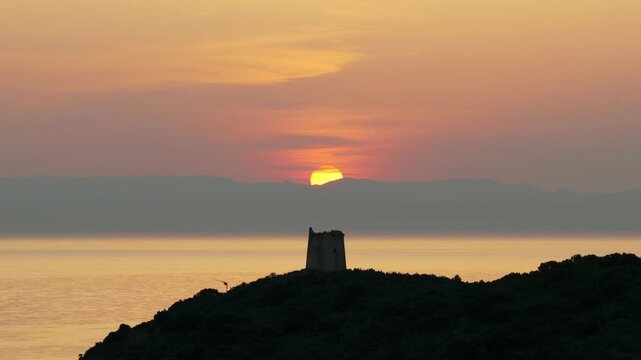 San Macario island and tower with setting sun in background, Pula, Sardinia, Italy. Aerial drone lateral view