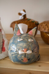 colorful ceramic cat sculpture sits proudly on wooden shelf. its playful features are highlighted by soft colors, surrounded by other handcrafted items, creating charming display. vertical. close up.