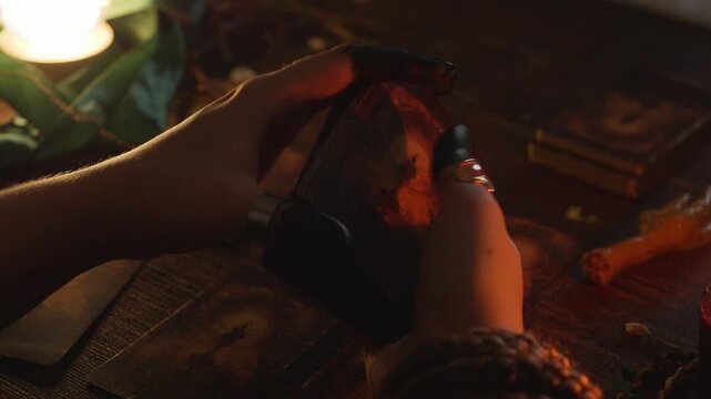 Fortune teller's hands holding and dealing dark, ancient tarot cards on a wooden table, performing a mystical divination ritual in a dimly lit, mysterious setting