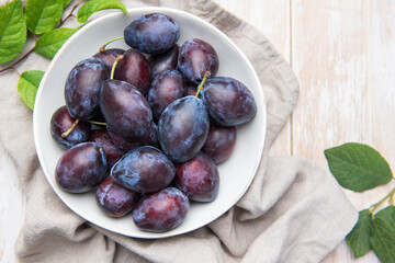 Fresh ripe plums in white bowl on table
