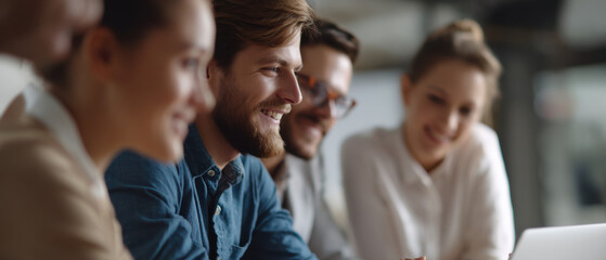 A group of young professionals smiling and working together around a laptop in a modern office setting.