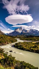 A river winds through a verdant valley, beneath dramatic mountains and a unique cloud formation