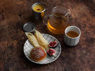 Cozy breakfast, snack - bun, cheese, figs, green tea and a candle on a wooden table