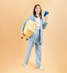 Happy Asian business woman holding passport and credit card with suitcase isolated on beige color background.