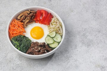 Bibimbap is a Korean dish in the form of a bowl of white rice topped with side dishes of vegetables, beef, eggs and spicy gochujang sauce.