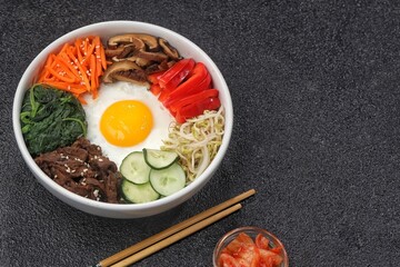 Bibimbap is a Korean dish in the form of a bowl of white rice topped with side dishes of vegetables, beef, eggs and spicy gochujang sauce.