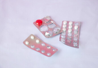 Three blister packs of medication on a light background. One pack contains white pills, another has a red pill, and the third has a mix of white and clear capsules.