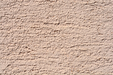 A full-frame close-up shows the rough, granular texture of a light beige or pale tan stucco wall with horizontal marks