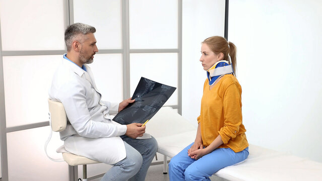 Orthopedist-traumatologist examines MRI images while female patient in neck brace sits attentively in medical office during check-up appointment - Powered by Adobe