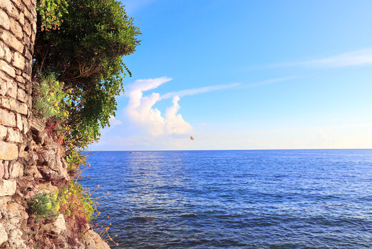 Picturesque view of sea, medieval wall and tourist on a parachute, Budva, Montenegro. Topic of summer vacation, leisure and adventure for tourist. A popular tourist pastime with a parasailing