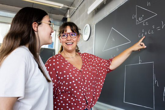 Smiling teacher explaining geometry on blackboard to student