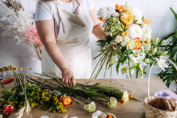 Florist creating a large wedding bouquet with orange and white blooms on a wooden table. Floral design process, seasonal weddings, rustic event planning, artisanal floristry