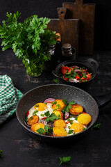 Fried eggs and potatoes with onions and chili peppers in a dark background.