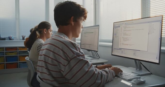 Male Student Learning Programming at Computer in Bright Classroom. Group Young People in IT Class Studying Software and Creating Game Development Projects. Teamwork, Technology Education. Dolly Shot.