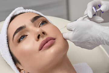 Beautician doing injections dermal fillers into female cheeks for a younger or more beautiful face. Cosmetology, filler treatment