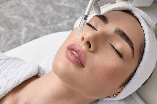 Lips filler injection for beautiful woman's lip augmentation with beautician on blue background. Lip augmentation procedure