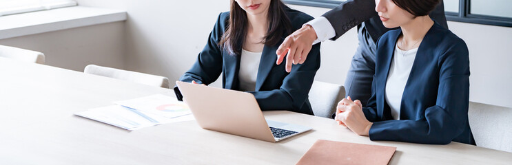 社内でパソコンを見て話をするスーツを着た男女