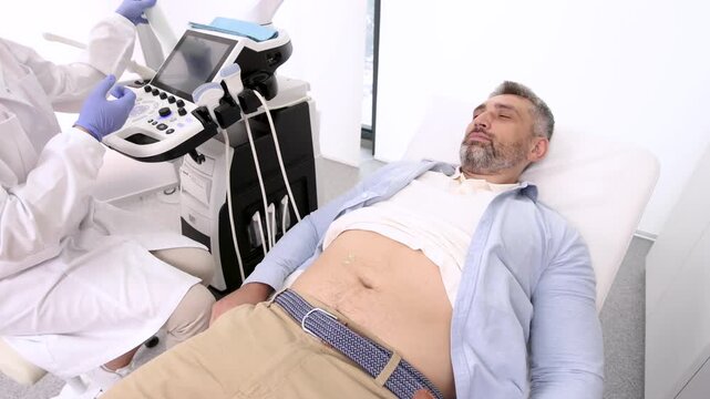 Ultrasound specialist doing ultrasonography of abdominal cavity for male patient with ultrasound machine at hospital