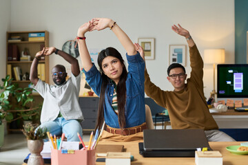 Diverse group of adults including Black man, Asian man, woman stretching arms together in modern office setting, in group exercise during work break
