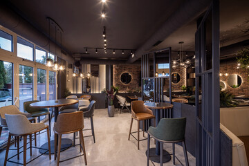 Modern restaurant interior with elegant furniture, warm lighting, exposed brick wall, and large windows providing natural light
