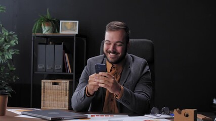 Happy businessman using smartphone at office desk - Powered by Adobe